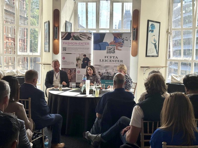 Liz sat at a table with 2 others, talking to the audience.